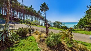 A coastal road with a wooden fence, lush greenery, and a clear view of the ocean. - Black Sands Escape- Ocean and Range Views- Comfort (Whitethorn)