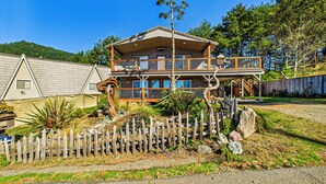 A two-story house with a balcony, surrounded by a wooden fence and various plants. - Black Sands Escape- Ocean and Range Views- Comfort (Whitethorn)