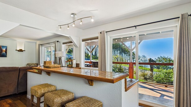 A modern kitchen with a bar area, large windows, and a view of the outdoors. - Black Sands Escape- Ocean and Range Views- Comfort (Whitethorn)