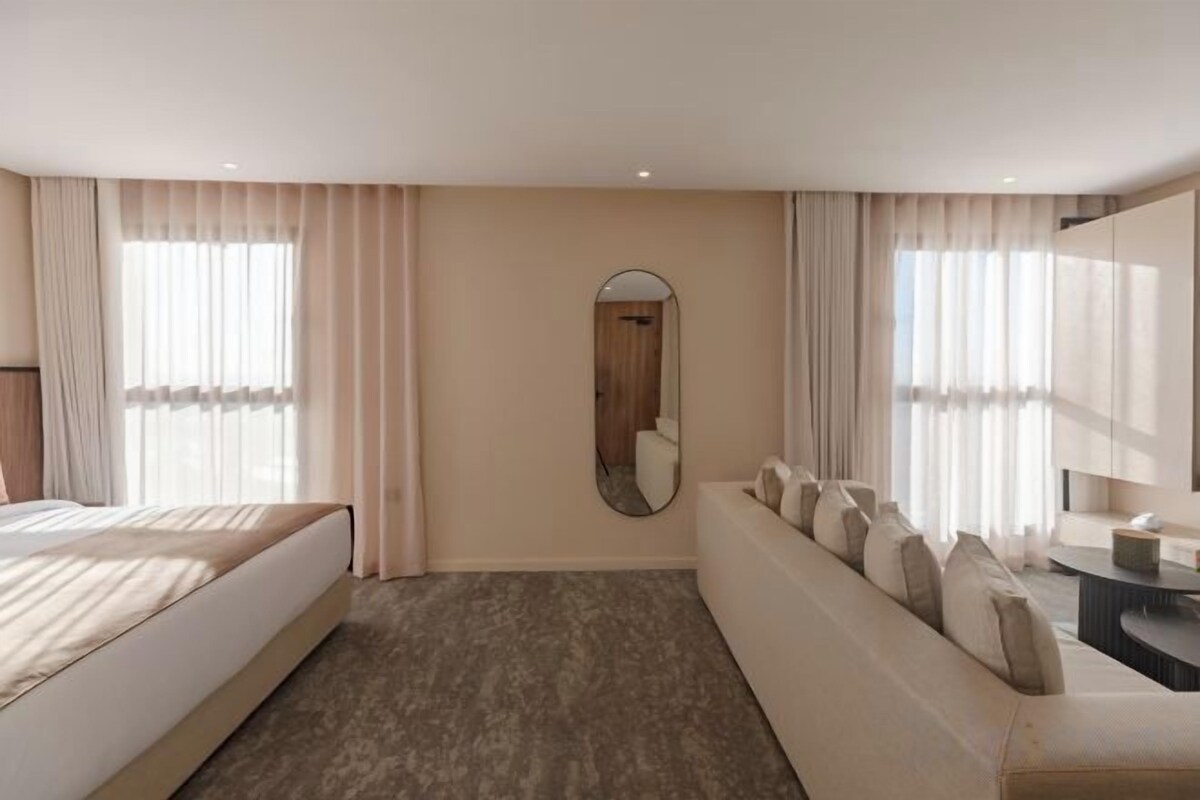 A hotel room with a bed, a sofa, a mirror, and a window with curtains.
