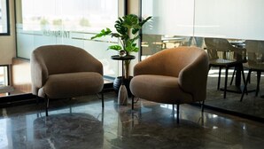 Two armchairs in a modern lobby with a glass wall, a potted plant, and a marble floor.
