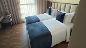 A hotel room with a large bed, a desk, and a window with curtains.