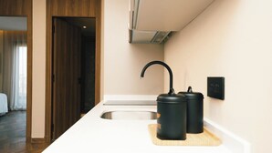 A modern kitchen with a white countertop, a sink, and two black kettles on a wooden board.