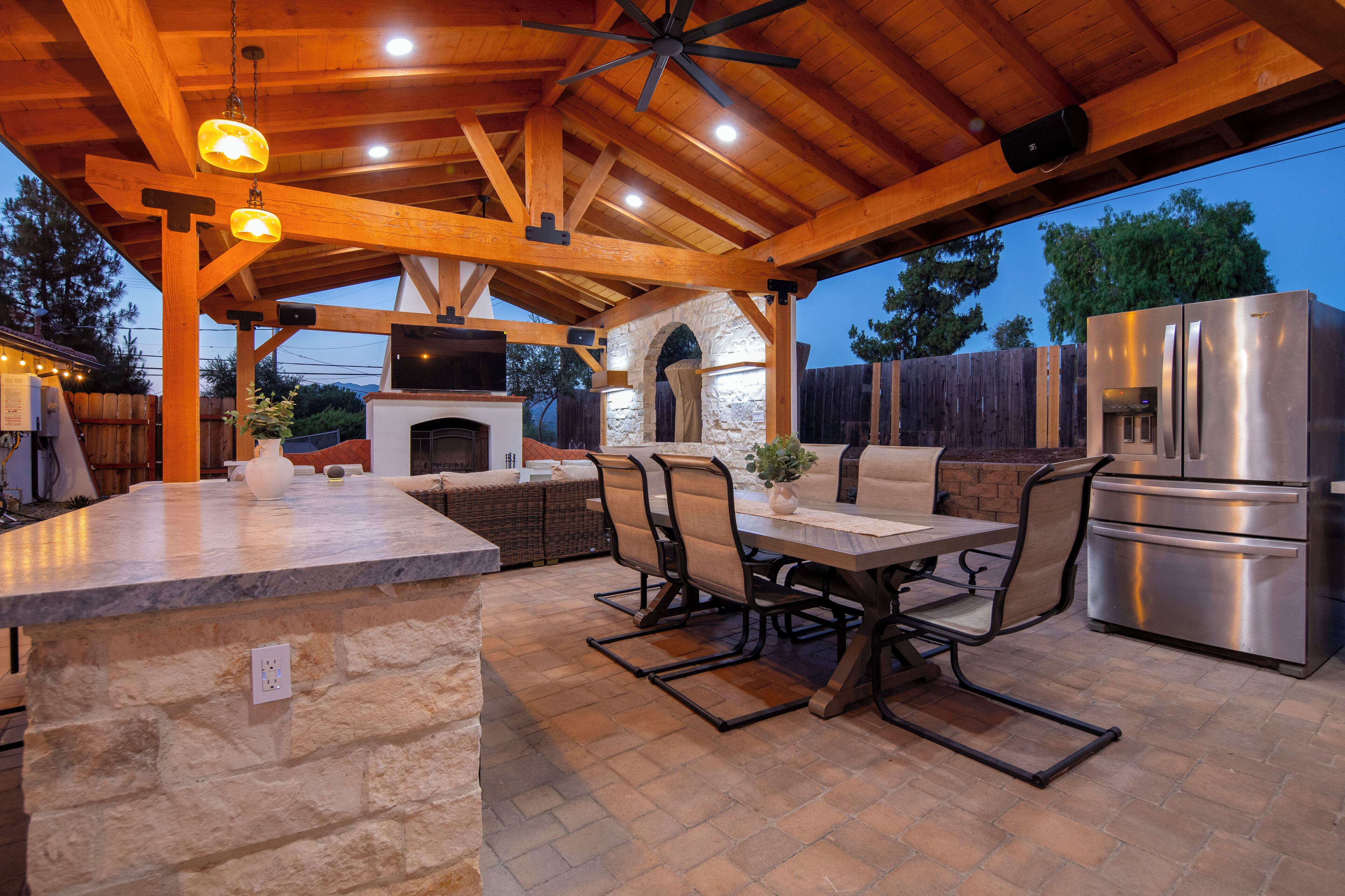 An outdoor kitchen area with a stone countertop, a grill, a refrigerator, and a seating arrangement.