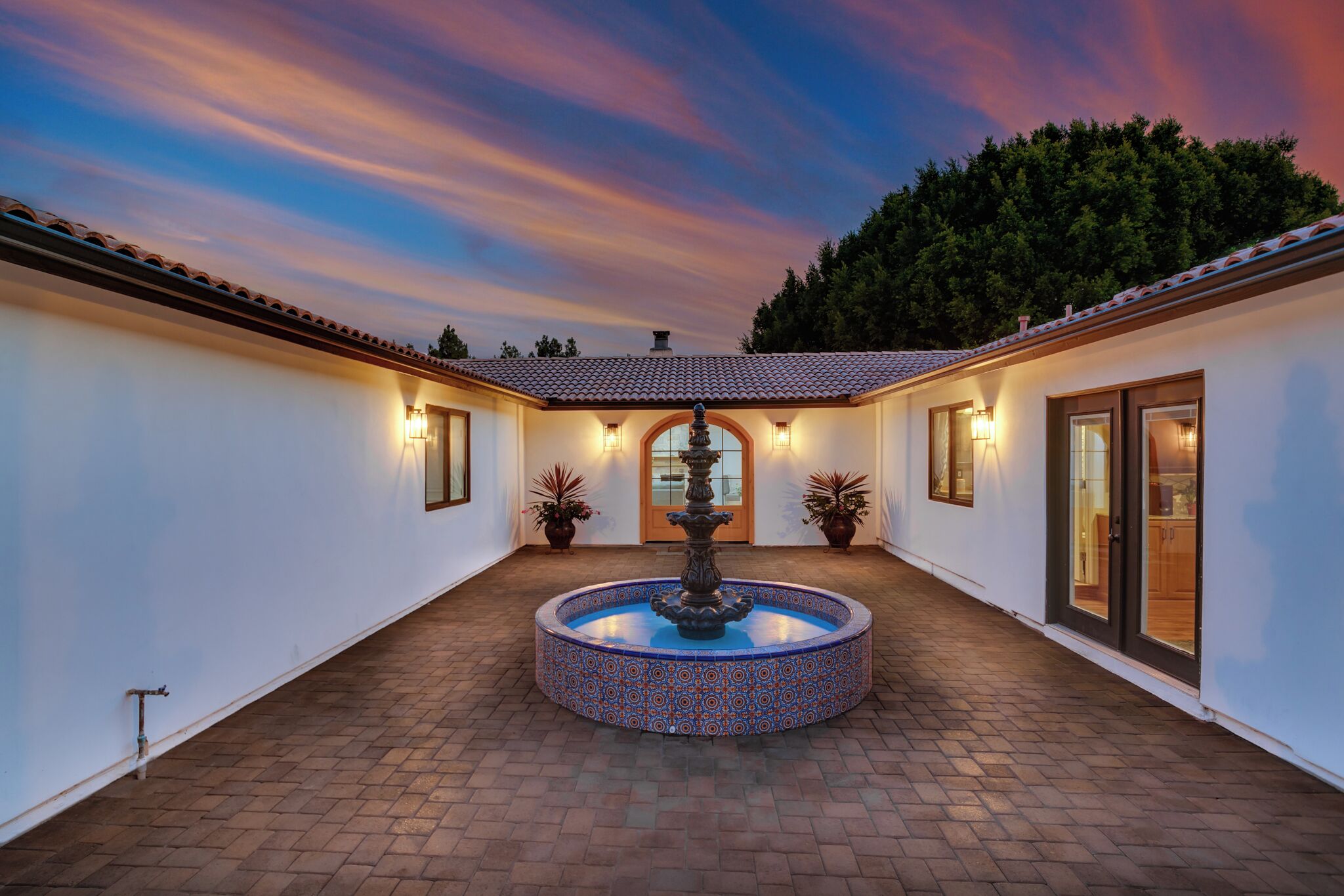 A courtyard with a central fountain, white walls, tiled roof, and potted plants.