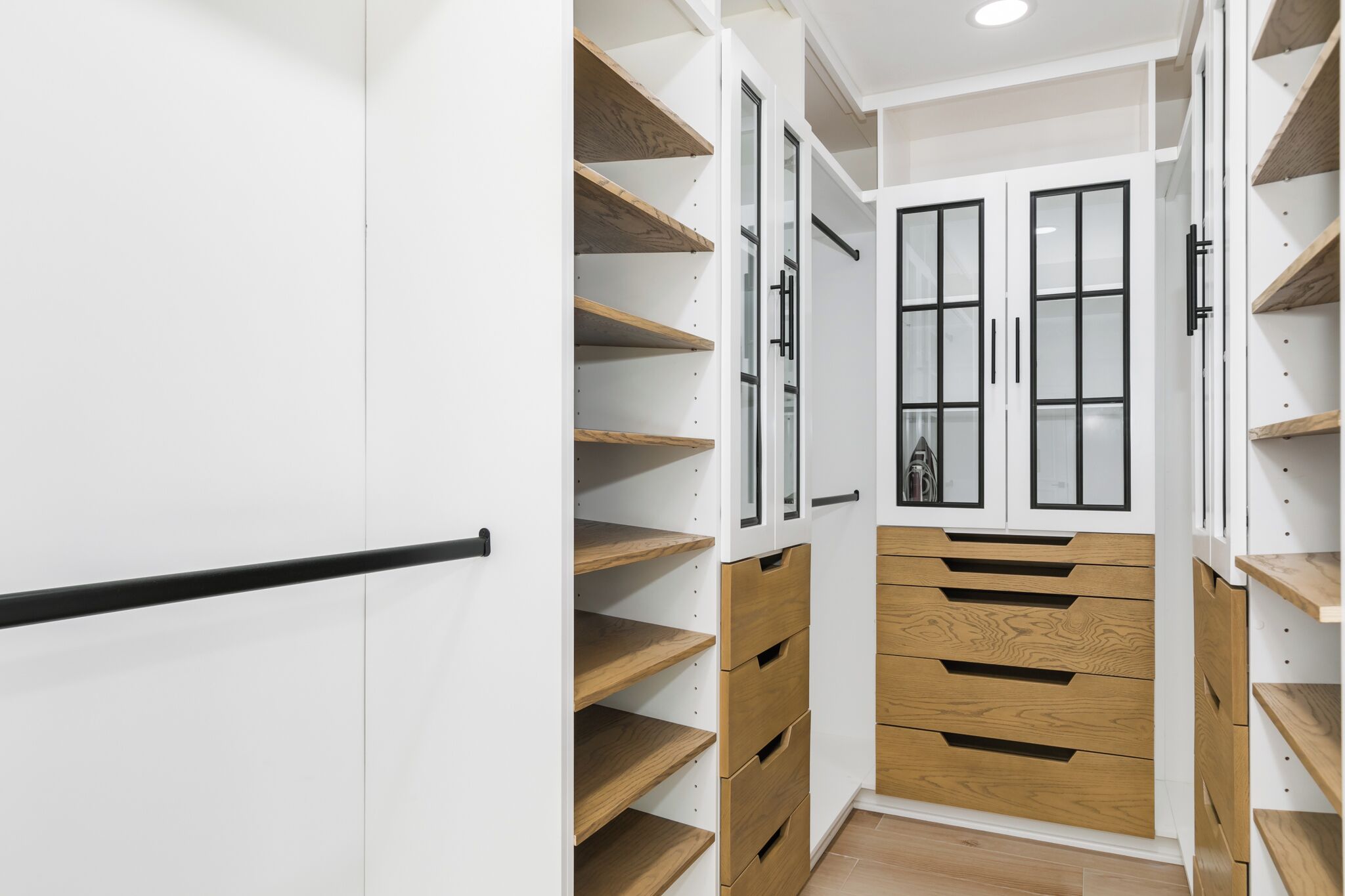 A narrow hallway with white walls, wooden shelves, and a central double door with a small window.
