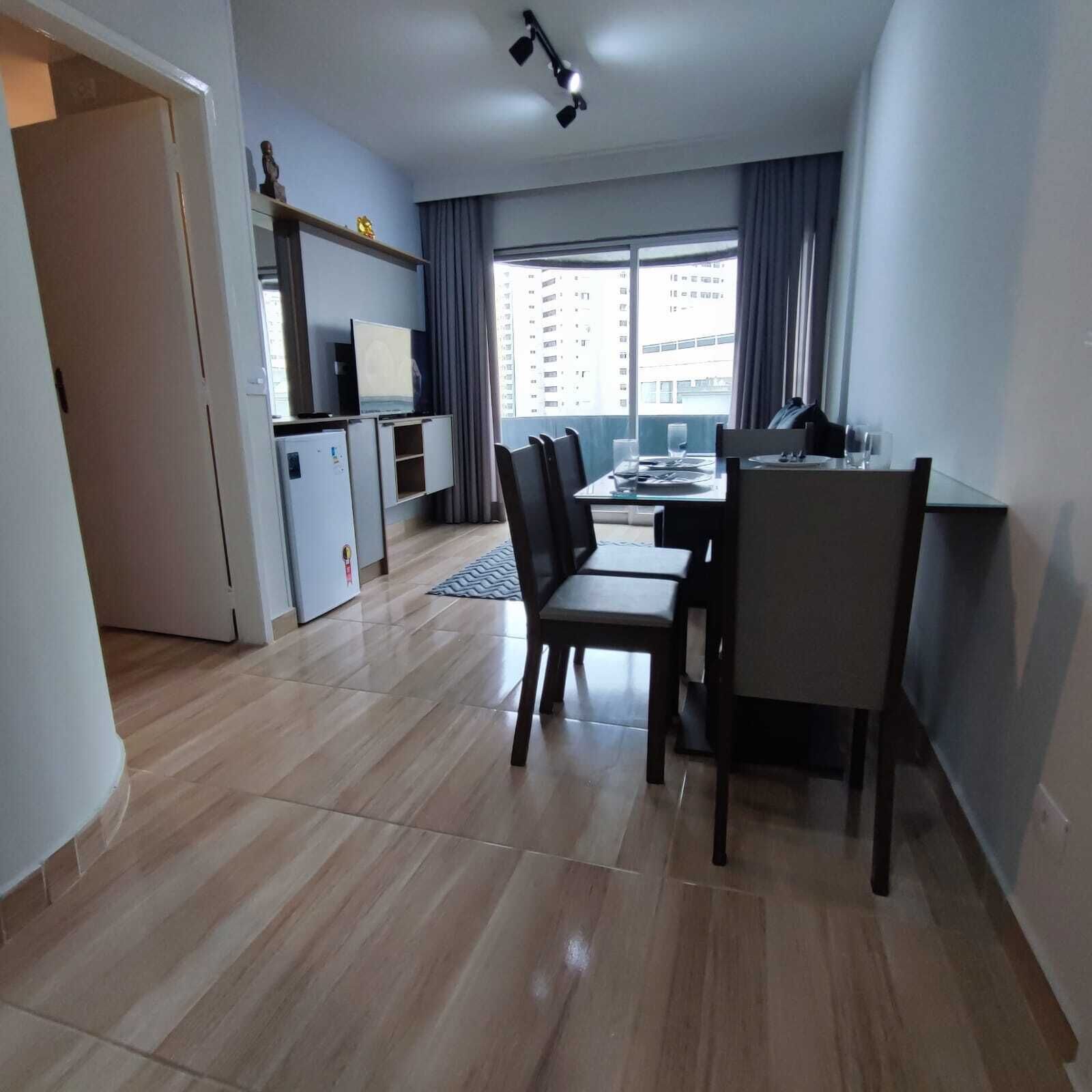 A modern living room with a dining area, a TV, and a small kitchenette.