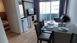 A modern kitchen with a dining area, a small refrigerator, and a television on a shelf. - APARTAMENTO FABULOSO LIBERDADE SP (São Paulo)