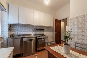 A kitchen with stainless steel appliances, a tiled backsplash, and a dining area with a table and chairs.