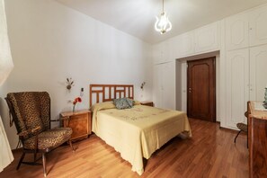A bedroom with a wooden bed, a leopard print chair, a nightstand, a wooden wardrobe, and a door.