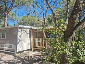 A small, single-story mobile home with a porch, surrounded by trees.