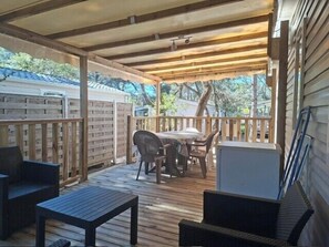 A covered outdoor patio with a table and chairs, a small table, and a refrigerator.