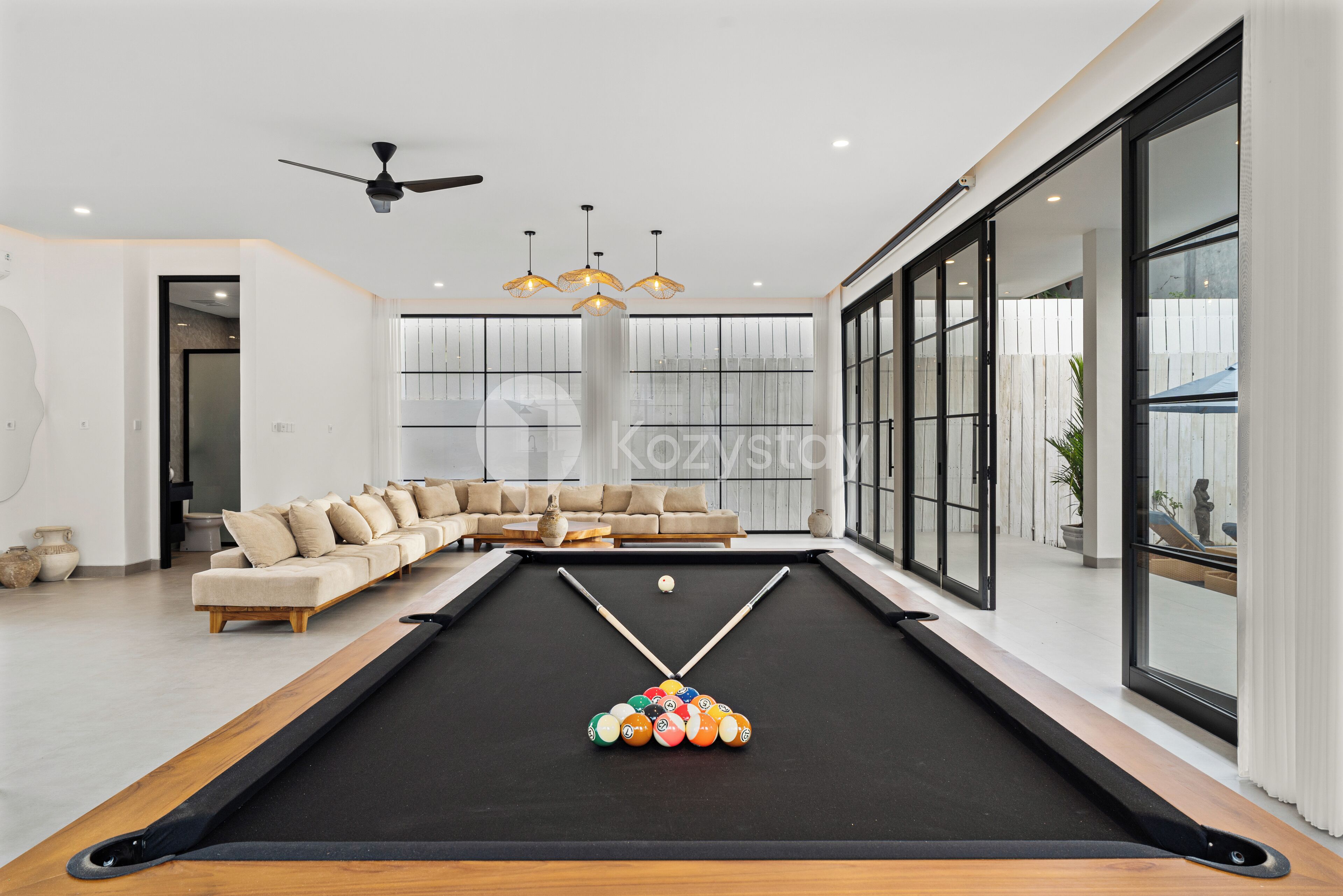A modern living room with a pool table, a sofa, and large windows.