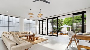 A spacious living room with a large sectional sofa, a wooden dining table, and a ceiling fan. - Kros Villa by Kozystay - Legian (Kuta)