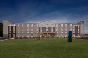 A multi-story hotel with a modern design, featuring a central entrance and a parking lot in front. - WoodSpring Suites Jackson Hub City (Jackson)