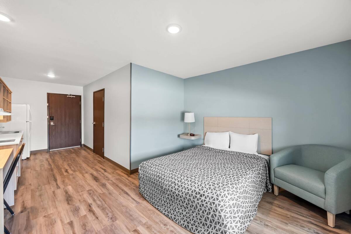 A hotel room with a bed, a sofa, a desk with a chair, a lamp, and a wooden door.