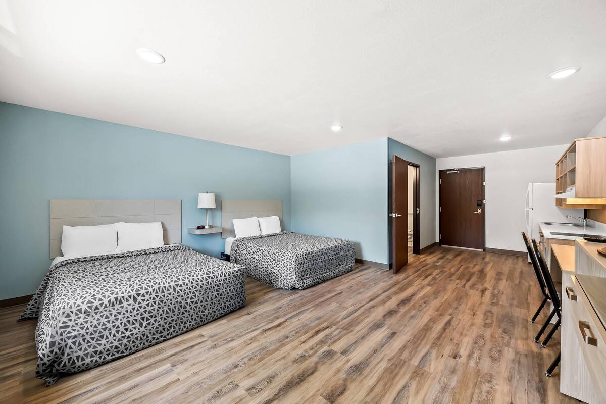 A hotel room with two beds, a desk, and a kitchenette.