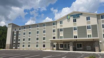 A multi-story hotel with a parking lot in front, featuring a modern design with a mix of grey and beige exterior walls and stone accents.