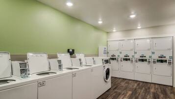 A laundry facility with multiple washing machines and dryers, green walls, and a wooden floor.