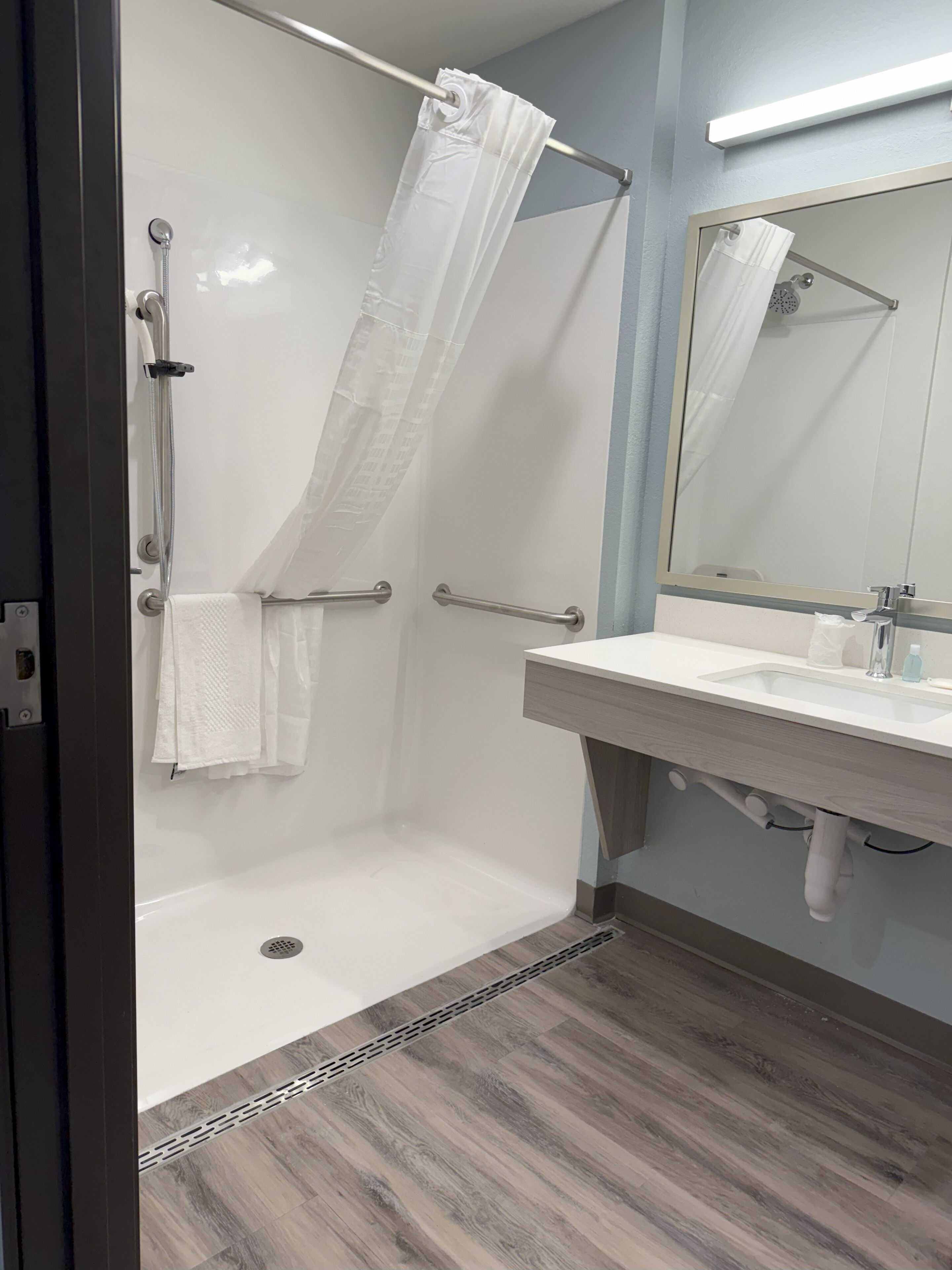 A modern bathroom with a walk-in shower, a vanity with a mirror, and a wooden floor.
