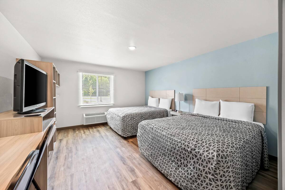 A modern hotel room with two beds, a TV, and a desk.