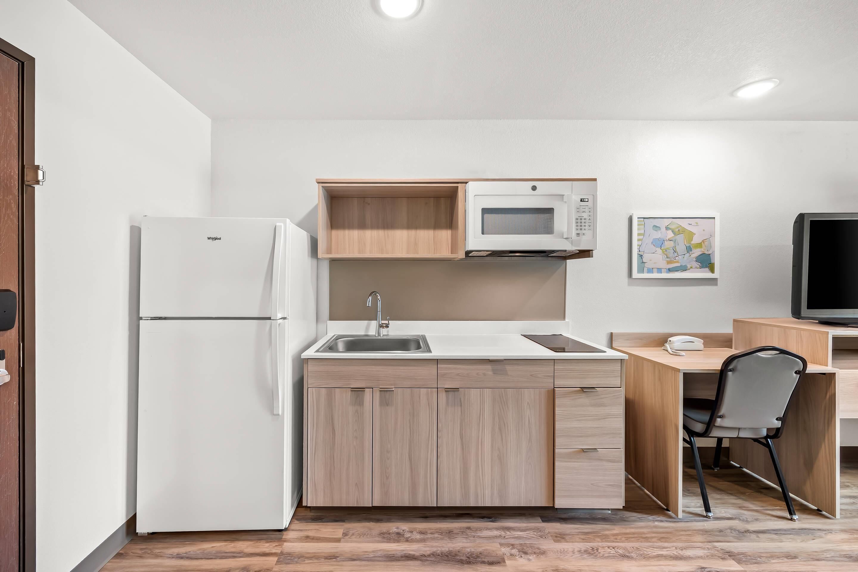 A compact kitchen with a refrigerator, microwave, sink, and wooden cabinets.