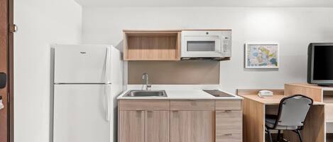 A compact kitchen with a refrigerator, microwave, sink, and wooden cabinets.