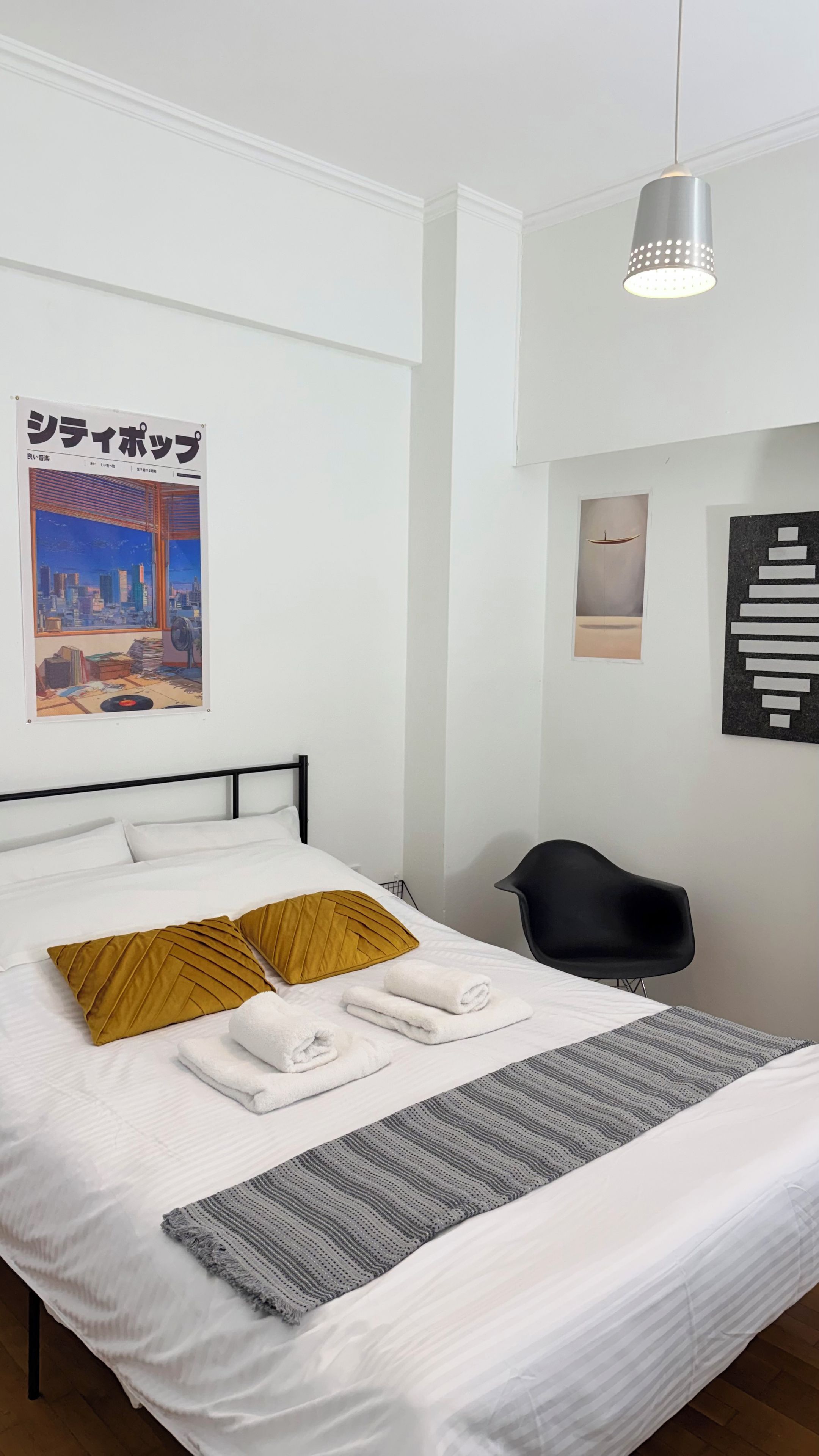 Ein ordentlich bezogenes Bett mit Kissen, ein Sessel und Bilder an den Wänden.