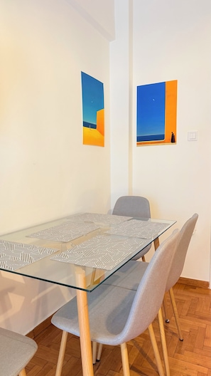 A room with a glass-top table, grey upholstered chairs, and two wall-mounted artworks depicting desert scenes.