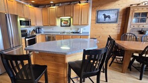 A kitchen with wooden cabinets, stainless steel appliances, a granite island, and a dining area with chairs. - Spacious Wisp Retreat w/ Views & Game Room (Mchenry)