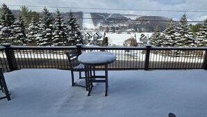 A snow-covered deck with a table and chairs, overlooking a residential area with houses and snow-covered trees. - Spacious Wisp Retreat w/ Views & Game Room (Mchenry)