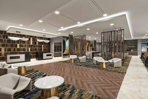 A modern lobby with a herringbone-patterned floor, a reception desk, seating area with sofas and tables, and a large bookshelf. - La Quinta Inn & Suites by Wyndham Shonto (SHONTO)