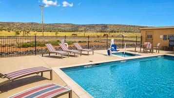 A swimming pool with lounge chairs and a fenced area with a view of a hilly landscape.
