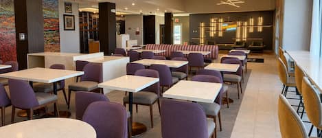 A modern restaurant with round tables and purple chairs, a bar area, and a mural on the wall.