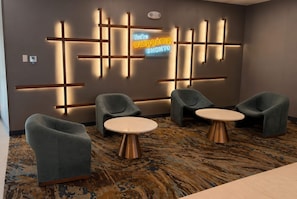 Zona de recepción de un hotel con diseño moderno, que incluye un letrero de neón, asientos y una alfombra estampada.