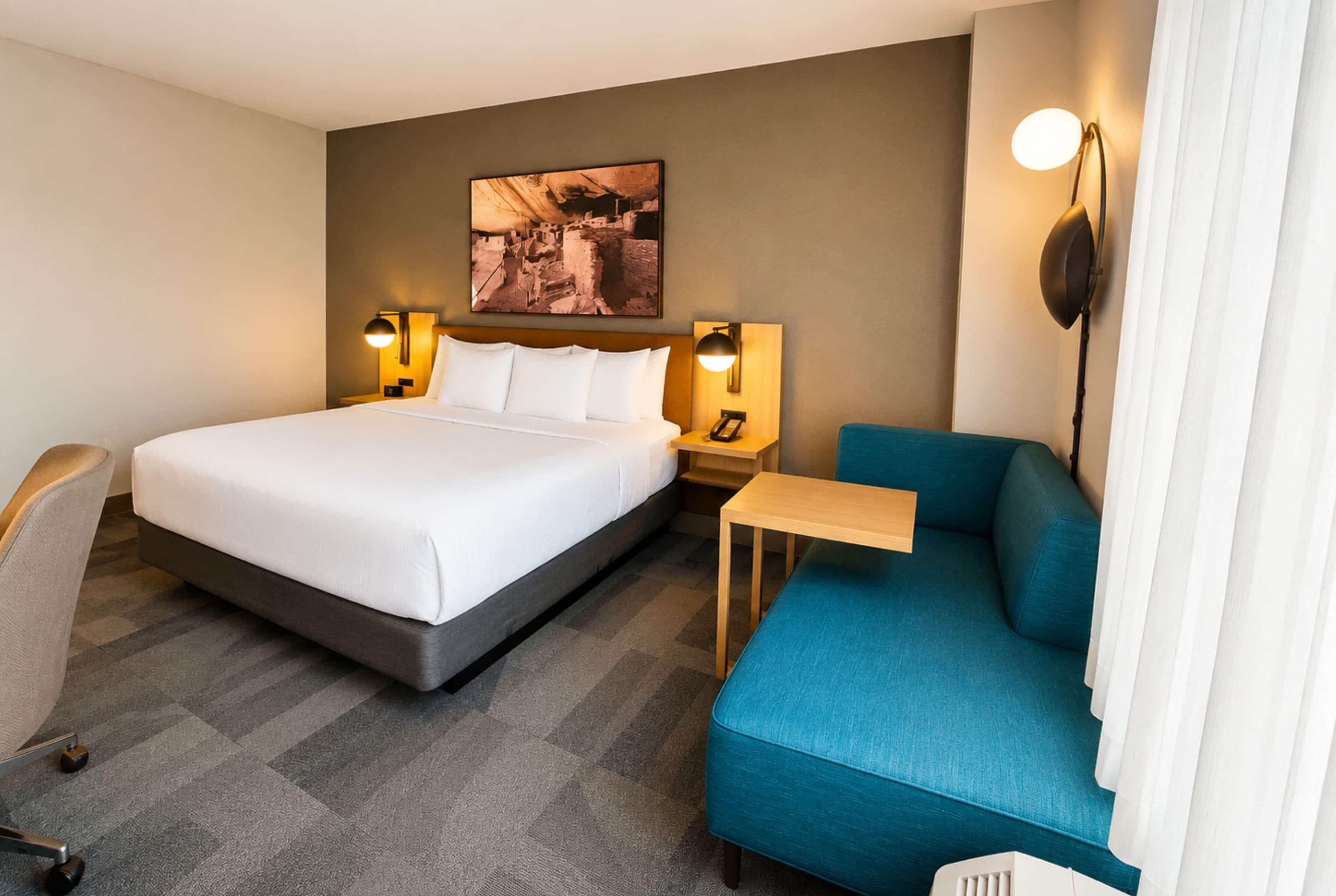 A hotel room with a bed, a desk, a chair, and a sofa.