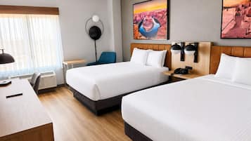 Een hotelkamer met twee bedden, een bureau, een stoel, een staande lamp en kunstwerken aan de muur.