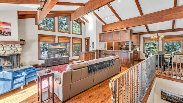 A spacious living room with a large sofa, a fireplace, and a kitchen area with wooden beams and large windows. - 3-Level Incline Village Retreat with Fireplace (Incline Village)