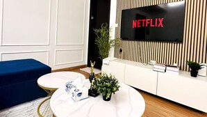 A modern living room with a flat-screen TV displaying 'NETFLIX', a blue sofa, a round coffee table, and a small plant.