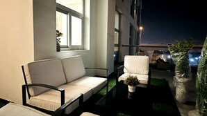 A modern outdoor seating area with white cushioned chairs and a sofa, a small table with a plant, and a view of the cityscape at night.