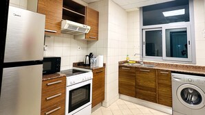 A modern kitchen with wooden cabinets, a stainless steel refrigerator, a built-in oven, a microwave, a sink, and a washing machine.