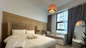 A spacious bedroom with a large bed, a bedside table, a nightstand, a window with curtains, and a hanging light fixture.