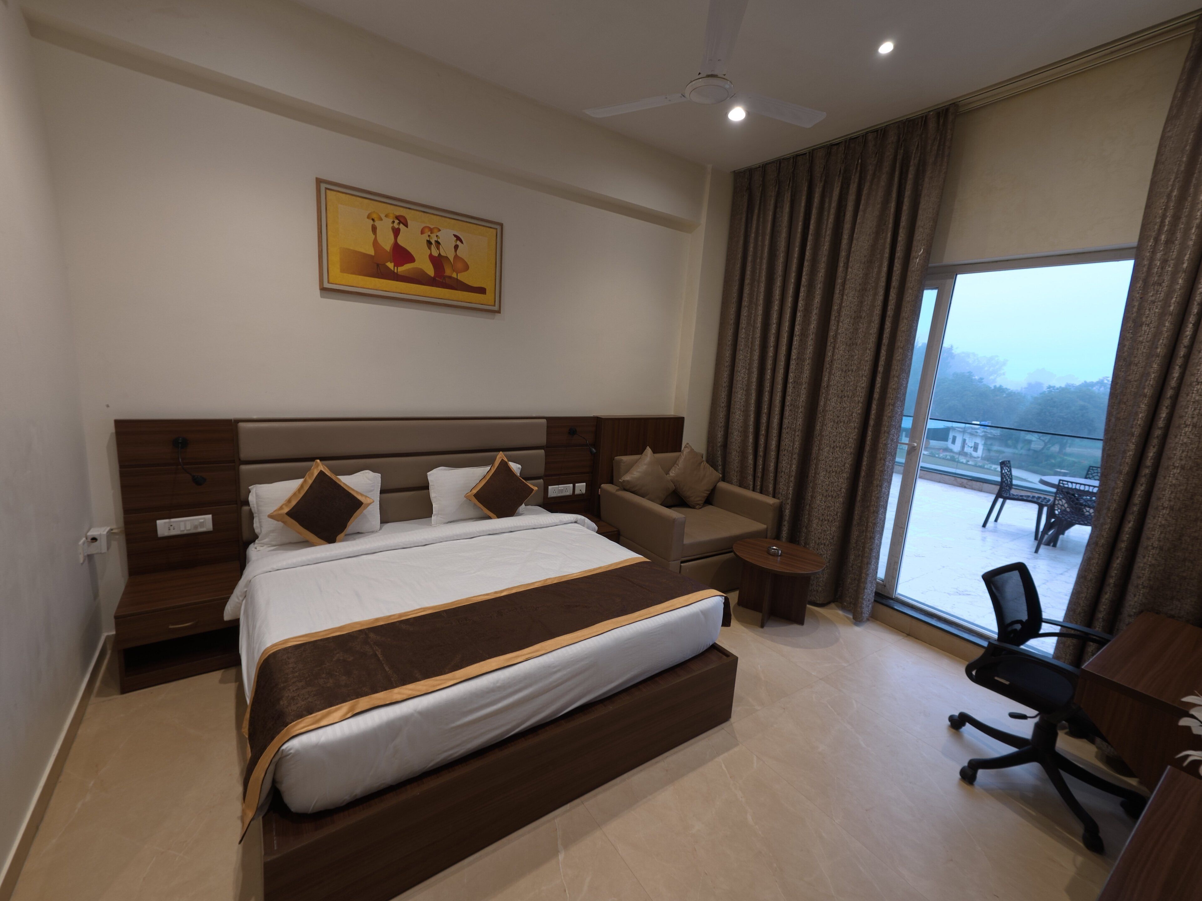 A modern hotel room with a large bed, a sofa, a small table, and a view of the outdoors.