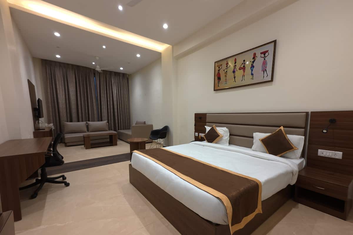 A modern hotel room with a large bed, a desk, a chair, a sofa, and a television.