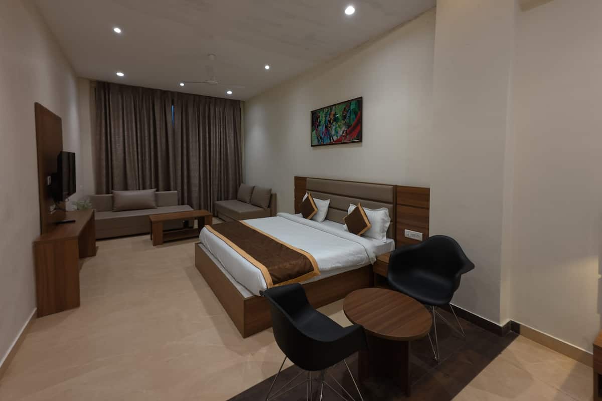A modern hotel room with a large bed, a sofa, a coffee table, and a TV.