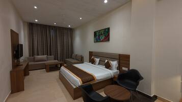 A modern hotel room with a large bed, a sofa, a coffee table, and a TV.