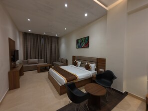 A modern hotel room with a large bed, a sofa, a coffee table, and a TV.
