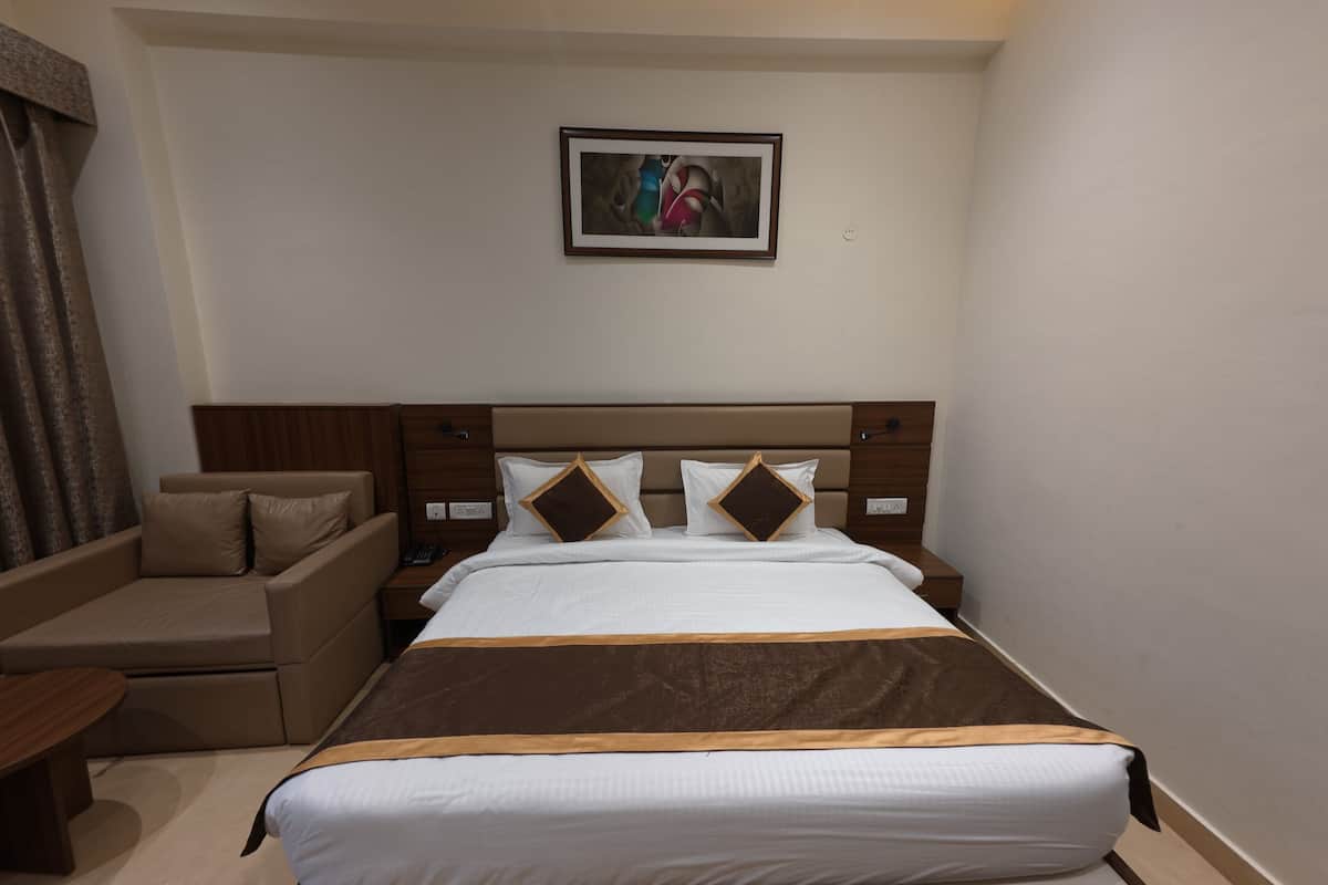 A hotel room with a large bed, a sofa, a bedside table, and a wall-mounted artwork.
