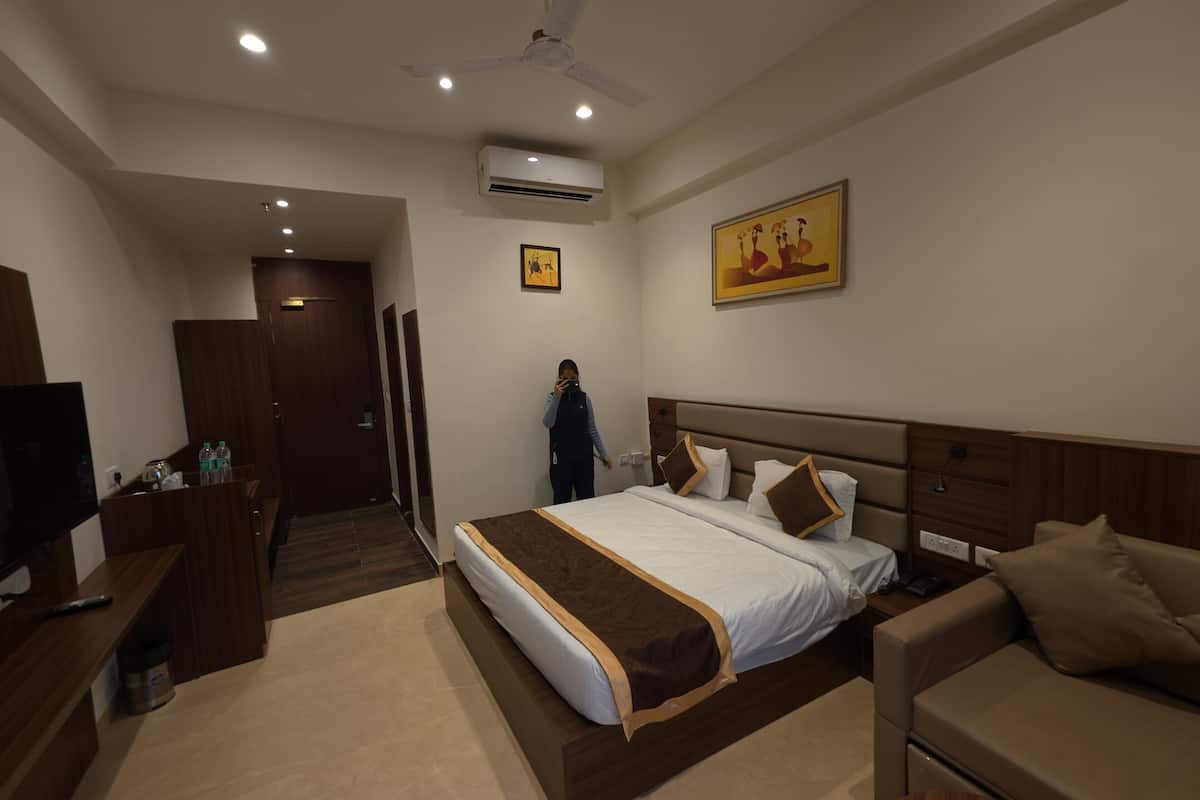 A hotel room with a bed, a sofa, a TV, a desk, and a ceiling fan.