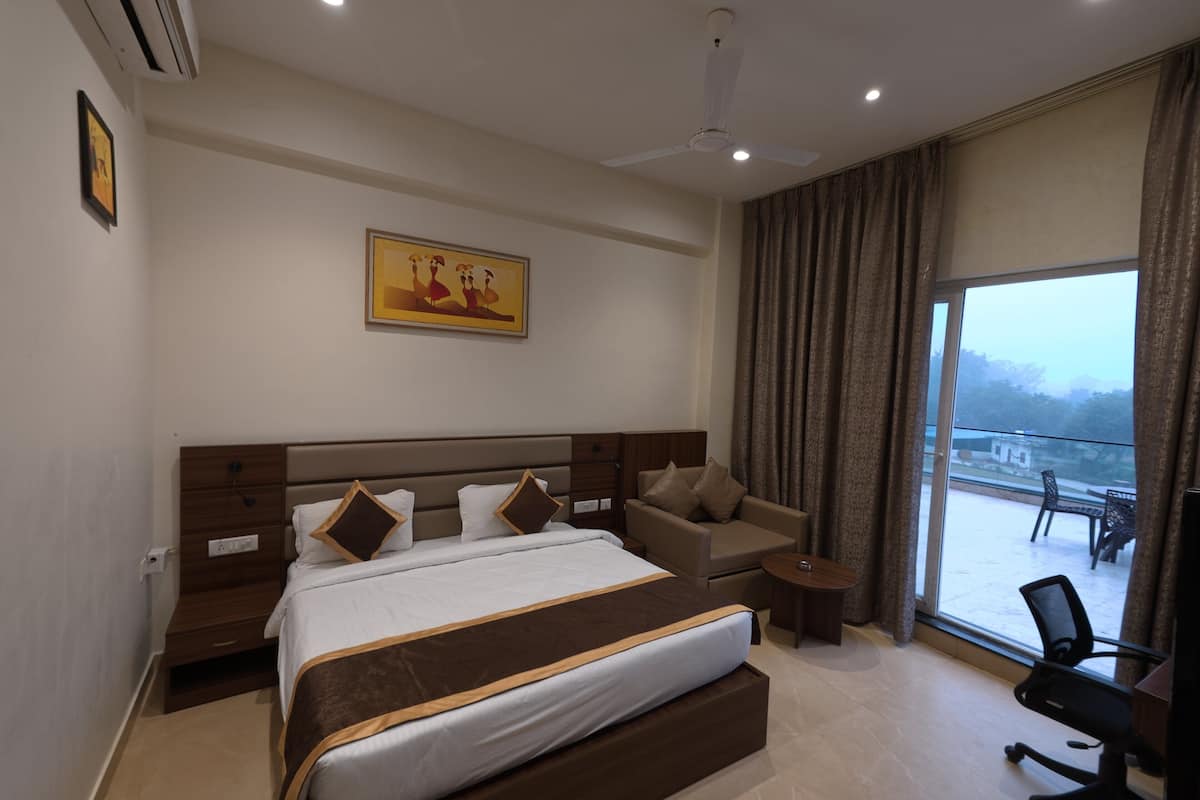 A hotel room with a large bed, a sofa, a small table, and a view of the outside.